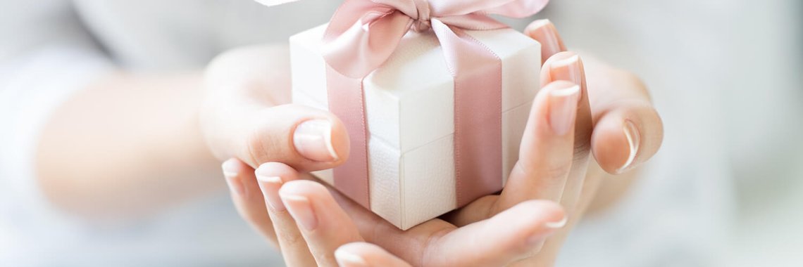 Close up shot of female hands holding a small gift wrapped with pink ribbon. Small gift in the hands of a woman indoor. Shallow depth of field with focus on the little box.